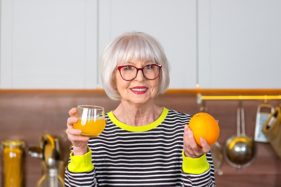 Mature woman holding an orange and a glass of orange juice, everyday sources of the vitamin C her eyes concentrate